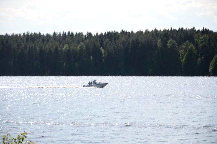Kaukana järvellä menevä vene. Taustalla metsämaisema.