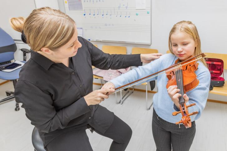 Aikuinen opettamassa lapselle viulun soittoa.
